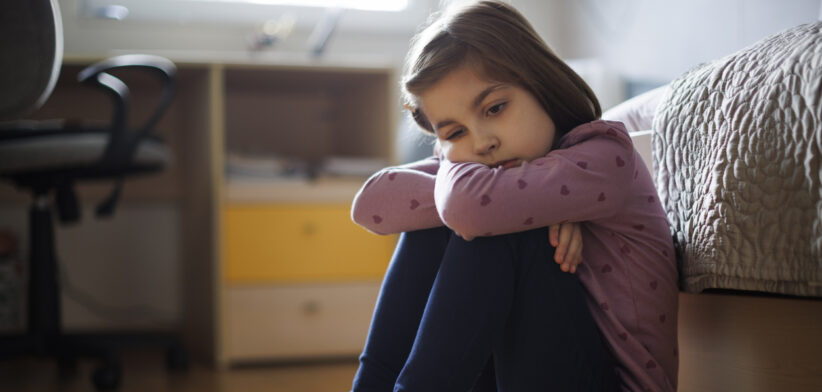Lonely little girl sitting alone on the floor at home