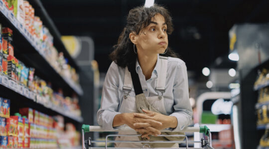 Young woman shopping in a supermarket, pushing a shopping cart through the aisles while browsing and selecting products. She is stocking up on weekly groceries, household cleaning supplies, and personal care items.