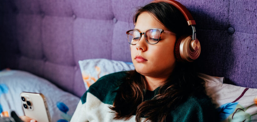 Teen girl relaxing in bed listening to music on smartphone