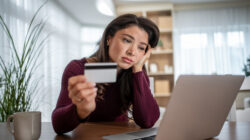 Woman experiencing financial stress holding credit card checking online banking
