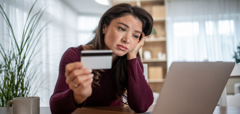 Woman experiencing financial stress holding credit card checking online banking