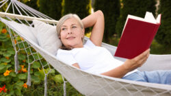 Senior woman with book resting in hammock outdoors