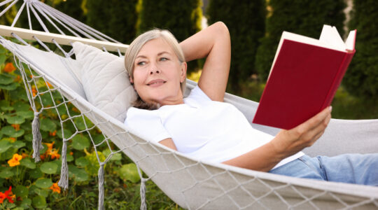 Senior woman with book resting in hammock outdoors