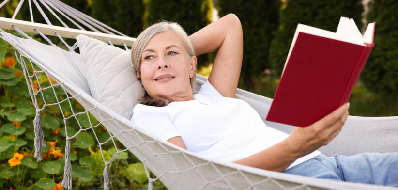 Senior woman with book resting in hammock outdoors
