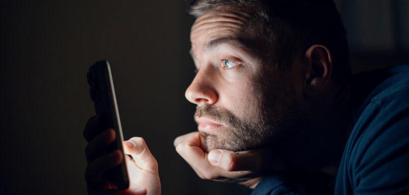 Man struggling with blue light smartphone addiction at night