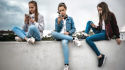 three teenage girls with smartphones on concrete wall