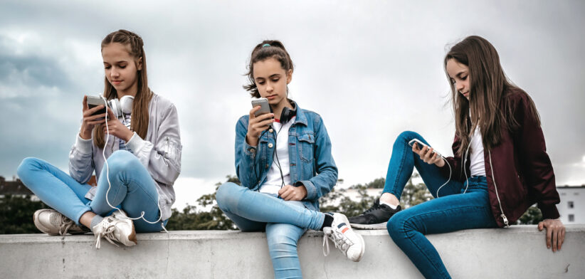 three teenage girls with smartphones on concrete wall
