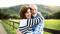 A senior couple hugging outdoors in nature.