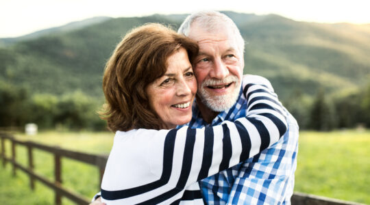 A senior couple hugging outdoors in nature.