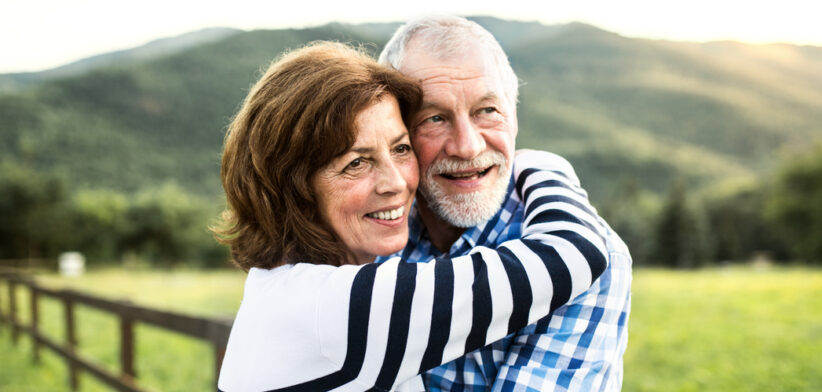 A senior couple hugging outdoors in nature.