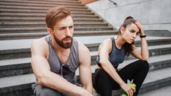Very tired couple is sitting on steps and having some rest. They have run a lot. Girl is keeping her hand close to the head while her boyfriend is just looking straight.