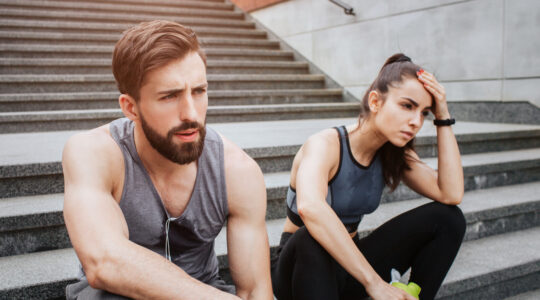 Very tired couple is sitting on steps and having some rest. They have run a lot. Girl is keeping her hand close to the head while her boyfriend is just looking straight.