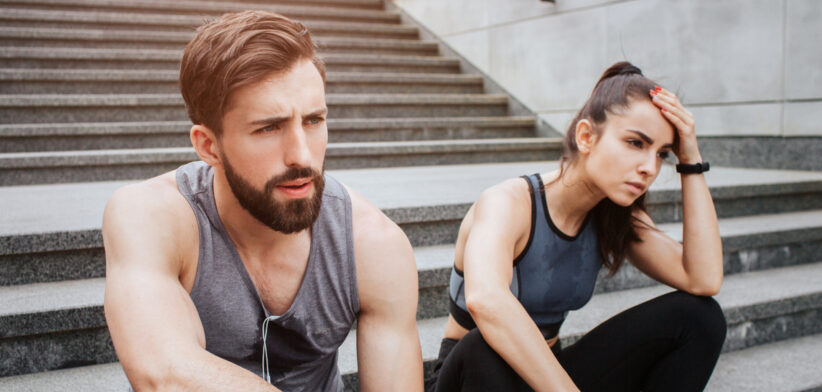Very tired couple is sitting on steps and having some rest. They have run a lot. Girl is keeping her hand close to the head while her boyfriend is just looking straight.