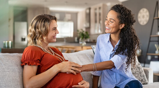 Excited friend touching belly bump of pregnant woman