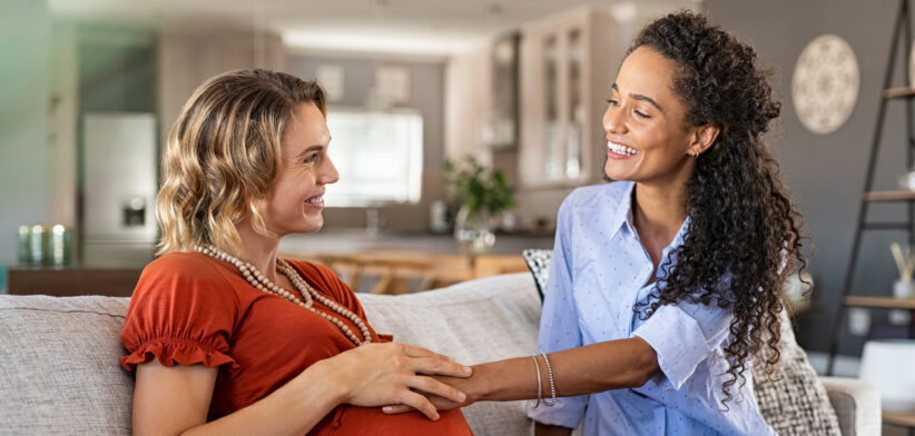 Excited friend touching belly bump of pregnant woman
