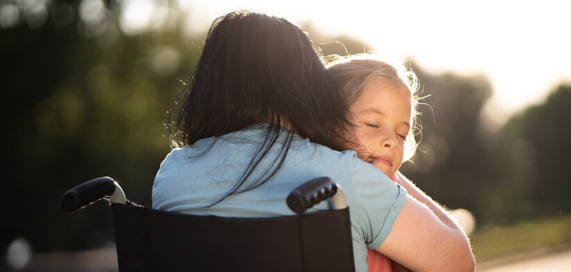 Child whit eyes closed embracing her mother in wheelchair