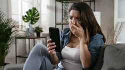 Sad woman sitting on the couch, using the phone