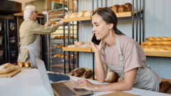 Busy female in apron using laptop and calling clients