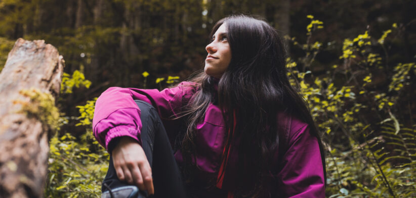 Happy girl resting on a fallen beech tree while hiking through the Irati forest (Navarre, Spain) in Autumn.