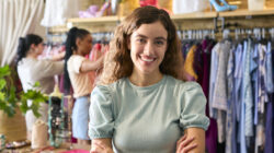 Portrait Of Female Owner Or Worker In Fashion Clothing Store With Customer In Background