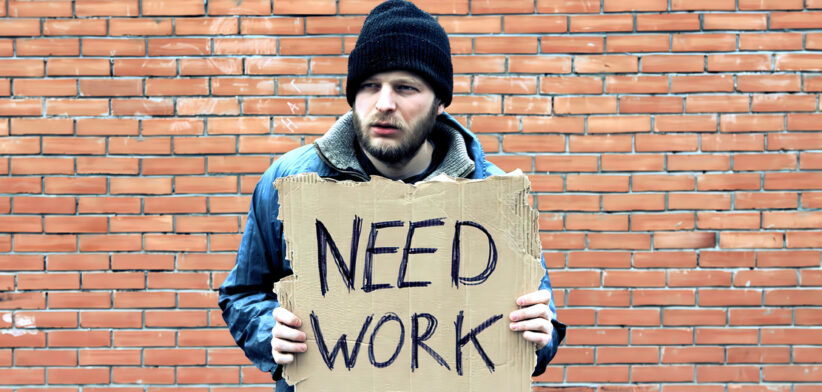 Homeless holds piece of cardboard with inscription Need Work. Refugee is at brick wall looking for job. Male tramp in dirty clothes. Below poverty line. Bearded fugitive beggar. Immigrant. Drunkenness
