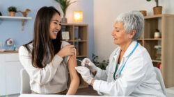 Female patient Japanese ethnicity receiving an annual flu vaccine, from the senior Caucasian female doctor