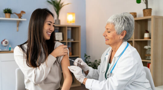 Female patient Japanese ethnicity receiving an annual flu vaccine, from the senior Caucasian female doctor