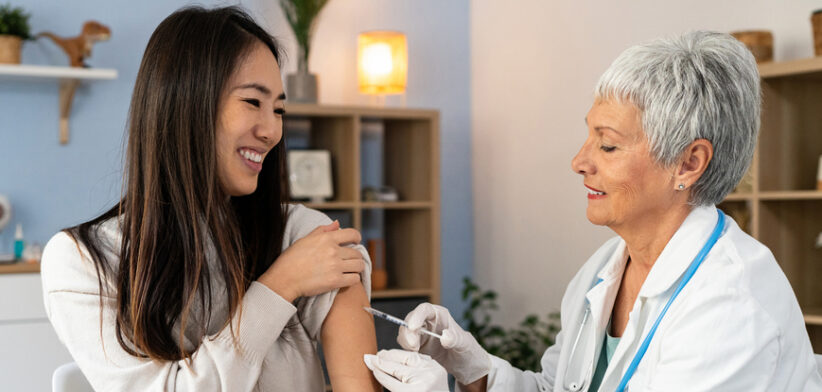 Female patient Japanese ethnicity receiving an annual flu vaccine, from the senior Caucasian female doctor