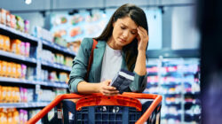 Mid adult woman feeling worried about grocery prices while shopping in a supermarket.