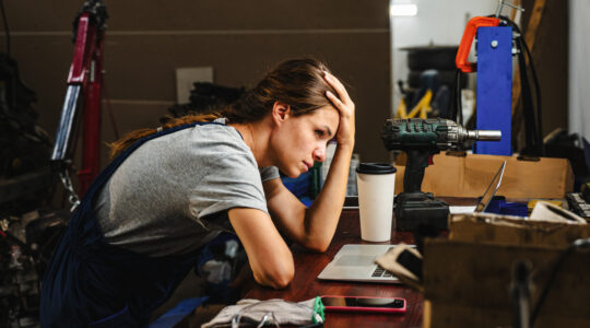 Worried woman entrepreneur in car service shop having business difficulties