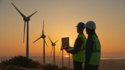 Engineers with Safety Helmets and Laptop at Wind Farm During Sunset, Focus on Renewable Energy, Sustainability, and Green Technology