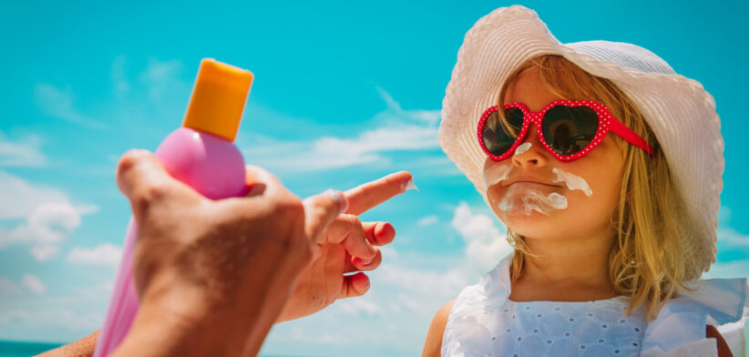 sun protection – mom put suncream on little girl face at beach