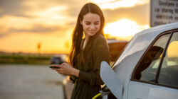 Woman waiting for electric car to charge in the parking lot at sunset