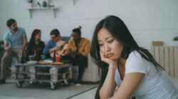 Young asian girl feels upset and isolated while her flatmates celebrating party at home indoors