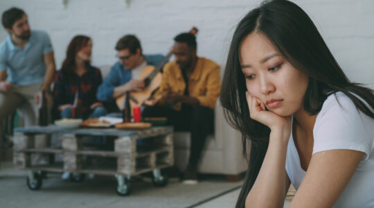 Young asian girl feels upset and isolated while her flatmates celebrating party at home indoors