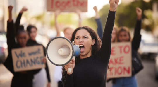 Woman, megaphone and fist in community protest for change, gender based violence or equality in the city. Angry women activist standing together in march strike for human rights or government action