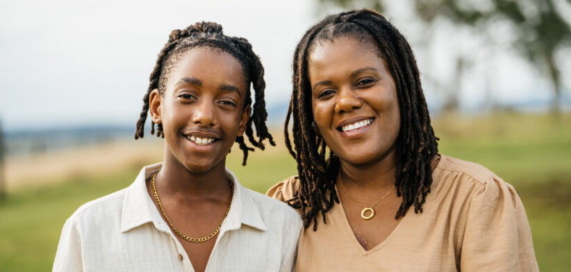 A joyful African mother and her smiling young son embracing outdoors in a sunny field, signifying warmth and love