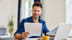 Happy man looking at document while working on laptop from home at living room