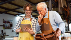 Senior artisan and apprentice crafting leather handbag in a workshop together