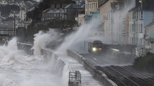 Local train leaving Dawlish station in a storm with waves breaking over it and the railway track