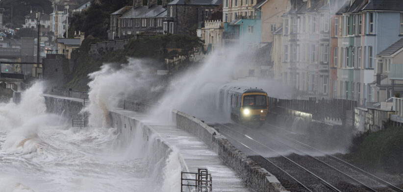 Local train leaving Dawlish station in a storm with waves breaking over it and the railway track