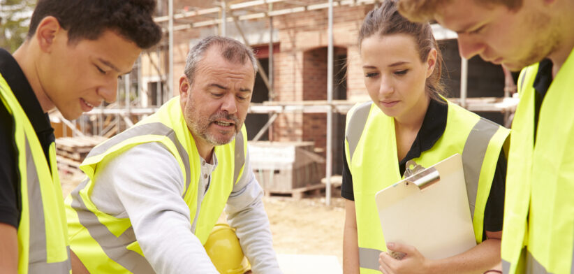 Builder On Building Site Discussing Work With Apprentice