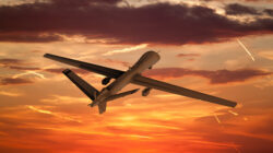 military UAV airplane flies against backdrop of beautiful view of the sunset sky orange with clouds and condensa