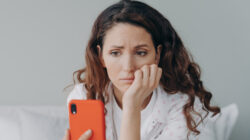 Stressed caucasian woman is doom scrolling. Girl reading morning news on smartphone in her bedroom.