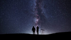 Fantasy landscape, two hiker standing on the hill, and looking at the Milky Way galaxy with telescope.