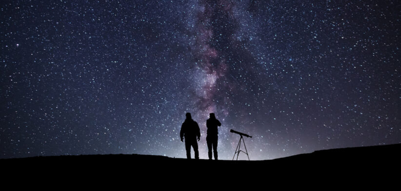 Fantasy landscape, two hiker standing on the hill, and looking at the Milky Way galaxy with telescope.
