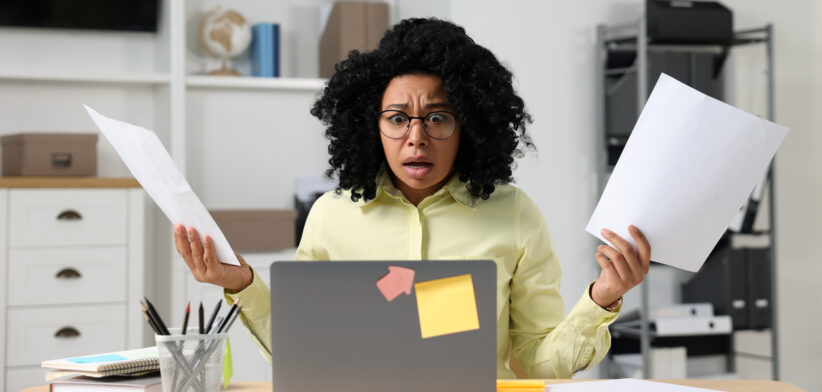 Deadline concept. Scared woman holding documents and looking at laptop in office