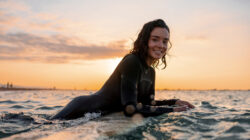 Young Adult Woman Resting On Her Surfboard Waiting For A Wave At Sunset