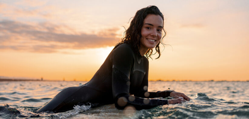 Young Adult Woman Resting On Her Surfboard Waiting For A Wave At Sunset