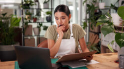 Woman, florist and clipboard with laptop at shop with stress, thinking and problem solving at small business. Person, pc and sustainability for plants with mistake, crisis and lost order on web store